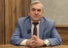 Профессор Александр Жаринов отмечает 85-летие Профессор Александр Жаринов отмечает 85-летие — портрет пожилого мужчины в голубом пиджаке и бордовом галстуке, сидящего за столом со сложенными руками, с петличным микрофоном на лацкане, на фоне деревянных панелей и серой стены, Meat Industry PRO