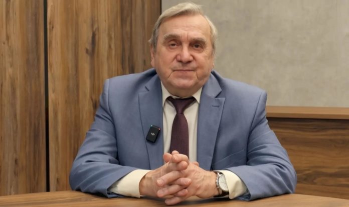 Профессор Александр Жаринов отмечает 85-летие Профессор Александр Жаринов отмечает 85-летие — портрет пожилого мужчины в голубом пиджаке и бордовом галстуке, сидящего за столом со сложенными руками, с петличным микрофоном на лацкане, на фоне деревянных панелей и серой стены, Meat Industry PRO