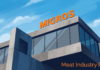 Централизованная вакуумная система Migros для упаковки мяса Централизованная вакуумная система Migros для упаковки мяса — современное здание мясоперерабатывающего предприятия Migros с крупной оранжевой вывеской на крыше, стеклянным фасадом и бетонными конструкциями; иллюстрация выполнена в графичной живописной манере на фоне голубого неба, логотип Meat Industry PRO оранжевым шрифтом в правом нижнем углу